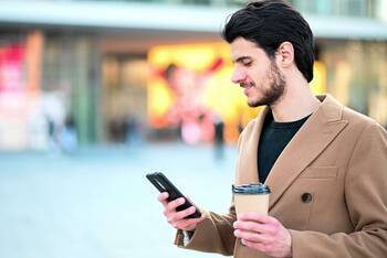Person steht draußen mit einem Kaffee und einem Smartphone in der Hand