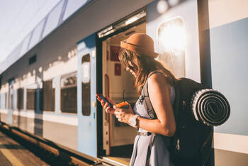 Frau steht vor Zug und guckt auf ihr Smartphone