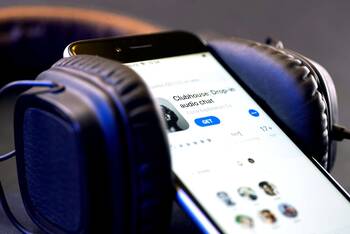 Smartphone mit Clubhouse App Anzeige im App Store zwischen Over Ear Kopfhörern