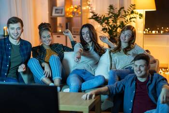 Fünf lächelnde Menschen sitzen auf Couch vor Fernseher