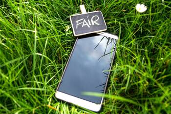 Smartphone liegt im Gras mit einer kleinen Tafel dabei, auf welcher "FAIR" steht
