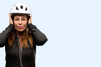 Frau mit aufgesetztem Fahrradhelm hält sich die Ohren zu