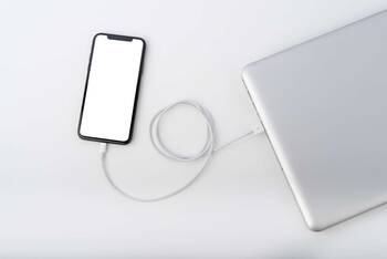 iPhone liegt an ein Notebook angeschlossen auf einem weißen Untergrund