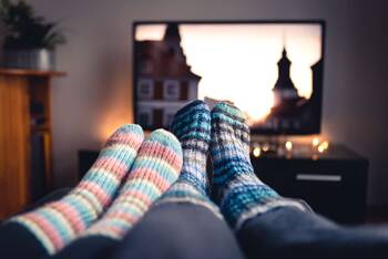 Zwei Paar Füße in Stricksocken vor Fernseher