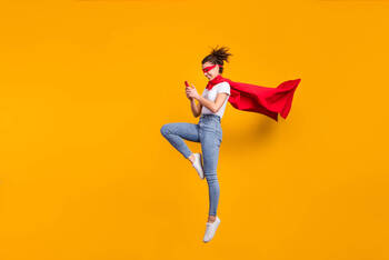 Frau im Superhelden Kostüm springt hoch mit Handy in der Hand