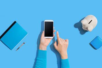 Zwei Hände halten Smartphone vor blauem Hintergrund mit Portemonnaie und Sparschwein