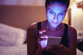 Junge Frau sitzt auf dem Bett und tippt am Smartphone