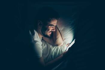 Person im Bett und in dunklem Raum bedient leuchtendes Smartphone