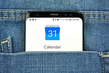 Smartphone mit Google Kalender Applikation ragt aus Jeans-Hosentasche