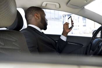 Mann sitzt mit Smartphone in der Hand im Auto