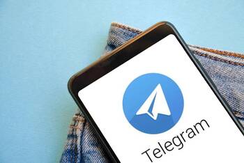 Smartphone mit Telegram Symbol und Schriftzug auf dem Display vor hellblauem Hintergrund