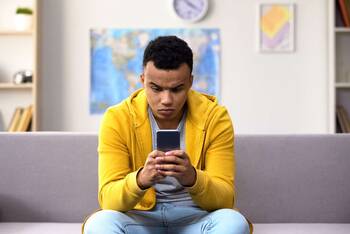 Ein Junge in gelber Jacke sitzt auf Sofa und schaut auf sein Smartphone