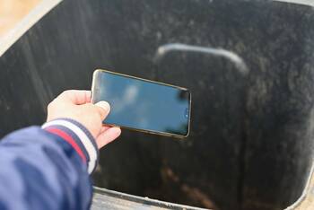 Hand schmeißt Smartphone in schwarzen Müllbehälter