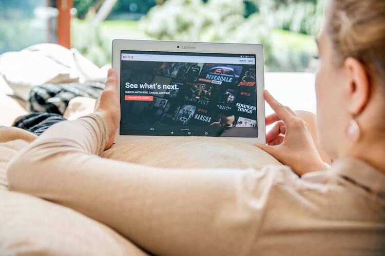 Frau sitzt auf Couch mit weißem Tablet mit Netflix Startseite auf Display