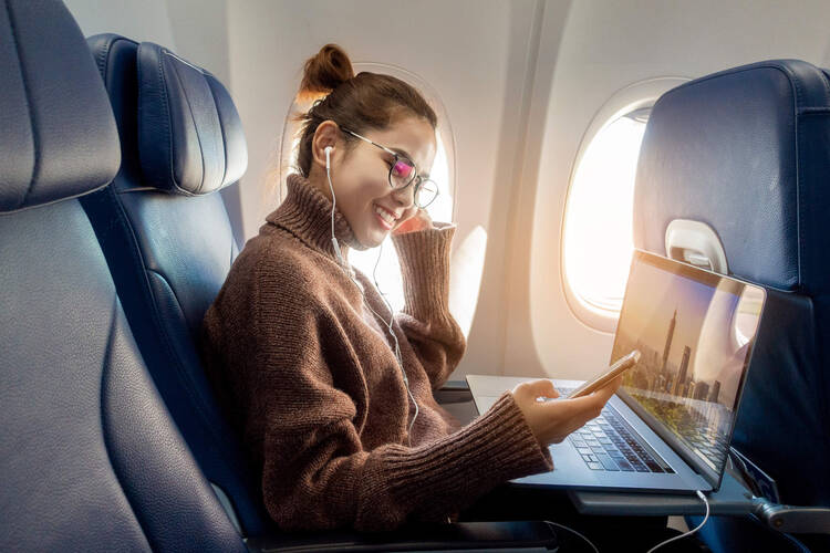 Frau sitzt mit Laptop im Flugzeug