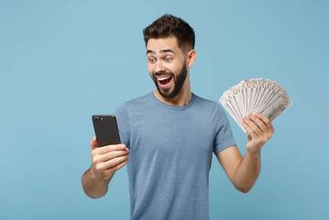 Mann guckt erfreut auf Smartphone, während er Geldscheine in der anderen Hand hält