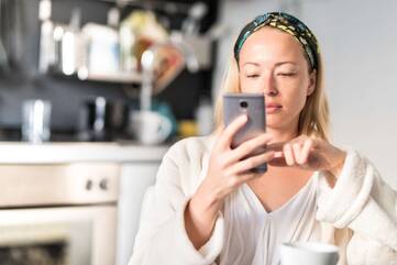 Frau sitzt in der Küche an ihrem Smartphone