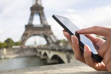 ein Smartphone wird vor dem Eiffelturm benutzt.