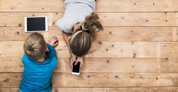 Mädchen und Junge liegen mit Tablet und Smartphone auf dem Boden