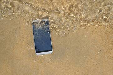 Smartphone liegt von Wasser umspült am Strand