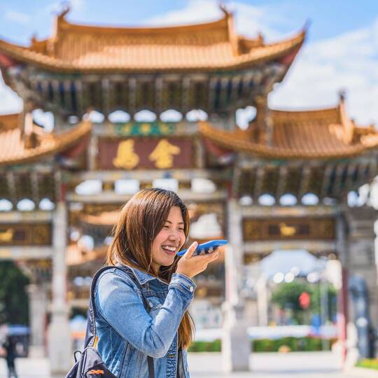 Frau steht vor chinesischem Gebäude und spricht in ihr Smartphone