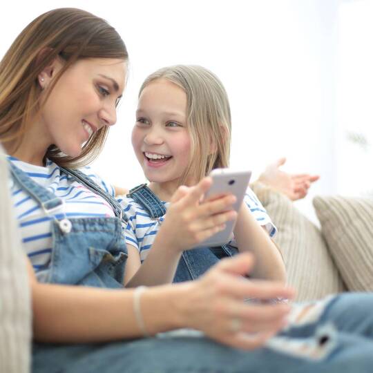 Mutter und Tochter sitzen auf dem Sofa und halten ein Smartphone in der Hand