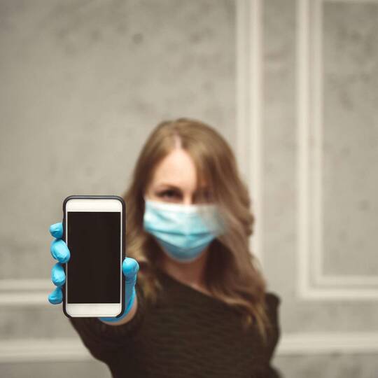 Frau mit Gesichtsmaske hält iPhone in die Kamera