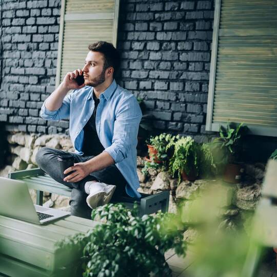 Mann sitzt auf Gartenbank und telefoniert mit dem Handy