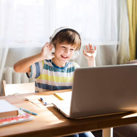 Kind sitzt fröhlich vor Laptop