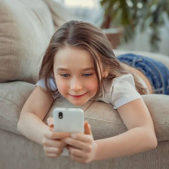Mädchen liegt auf der Couch und bedient ihr Smartphone