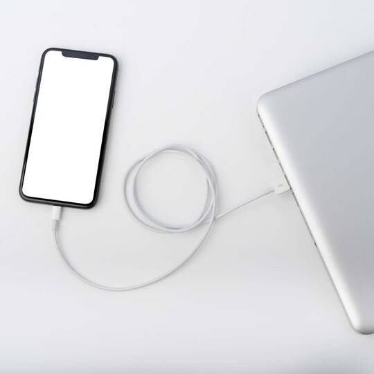 iPhone liegt an ein Notebook angeschlossen auf einem weißen Untergrund