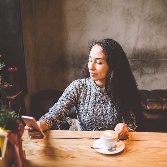 Frau in Café schaut auf Smartphone