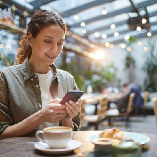 Frau sitzt in Café und schaut auf Smartphone