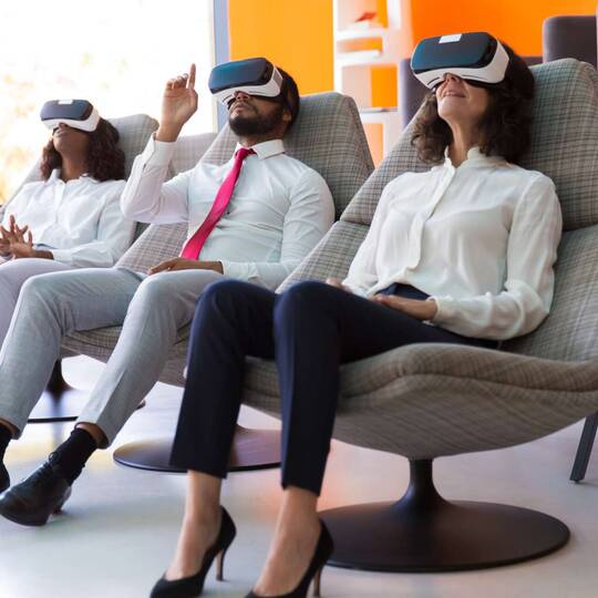 Drei Personen sitzen mit VR-Brille auf Sesseln