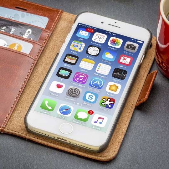 Entsperrtes iPhone in einer Lederhülle neben einer Tasse Kaffee