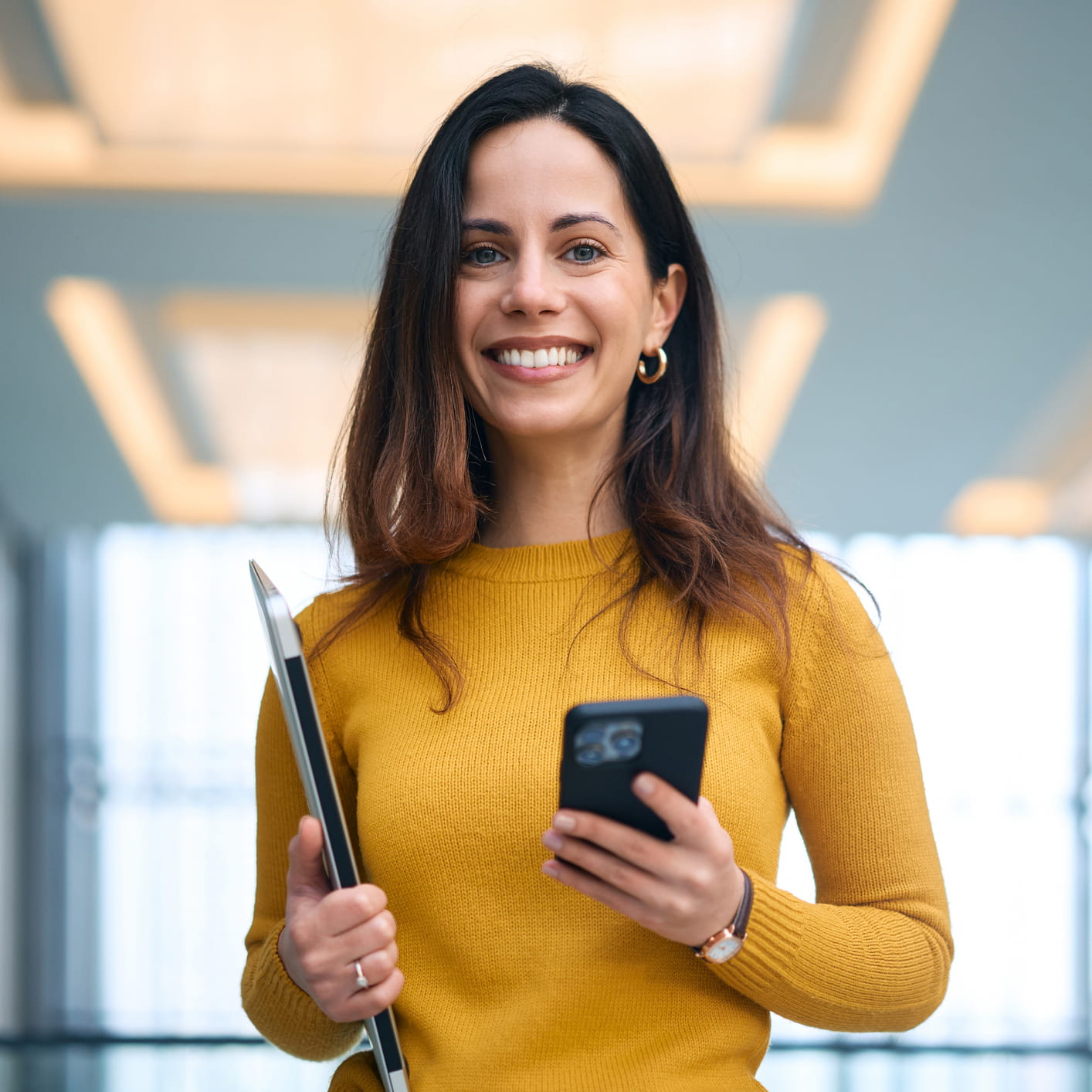 Frau in gelbem Oberteil mit Handy in der Hand