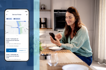 Eine Frau steht in der Küche, schaut auf ihr Smartphone und lächelt