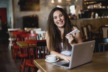 Frau mit Handy in der Hand sitzt lächelnd an Tisch im Café