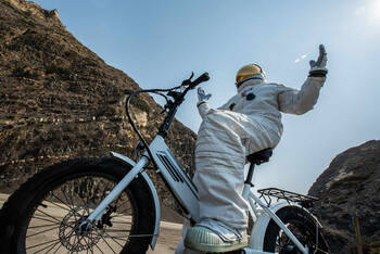 Astronaut sitzt auf einem Fahrrads mit Metallreifen