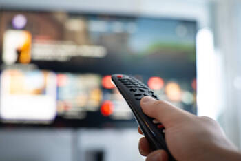 Eine Person hält eine Fernbedienung in Richtung des Fernsehers.