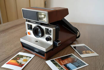 Eine Sofortbildkamera steht auf dem Tisch und um sie herum liegen einige geschossene und ausgedruckte Bilder.