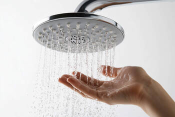 Eine Person hält die Hand unter den laufenden Duschkopf.