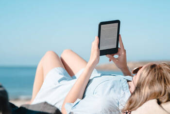Eine Frau liegt am Strand und liest in einem E-Book-Reader.