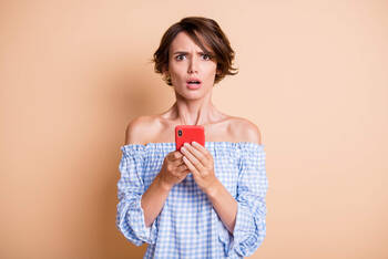 Eine Frau blickt verdutzt, während sie ihr Handy in der Hand hält.