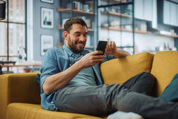 Ein Mann sitzt auf dem Sofa und schaut auf sein Smartphone.