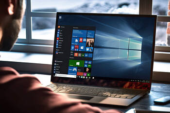 Ein Mann sitzt vor einem Notebook und blickt auf den Windows-Desktop.