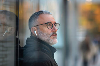 Ein Mann lehnt sich an eine Fensterscheibe und hört dabei Musik über seine AirPods.