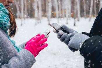 Zwei Personen an ihren Handys mit Handschuhen in einer Winterlandschaft