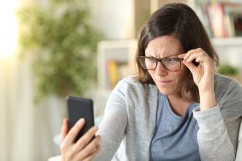 Eine Frau mit Brille schaut skeptisch auf ein Smartphone.