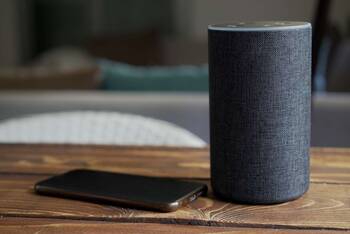 Auf Holztisch liegen Smartphone und Alexa-fähiges Gerät